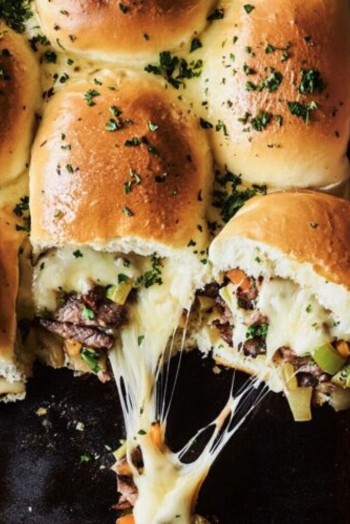 Pulling a cheesy ribeye steak slider from a tray, a standout example of cookout side dishes.
