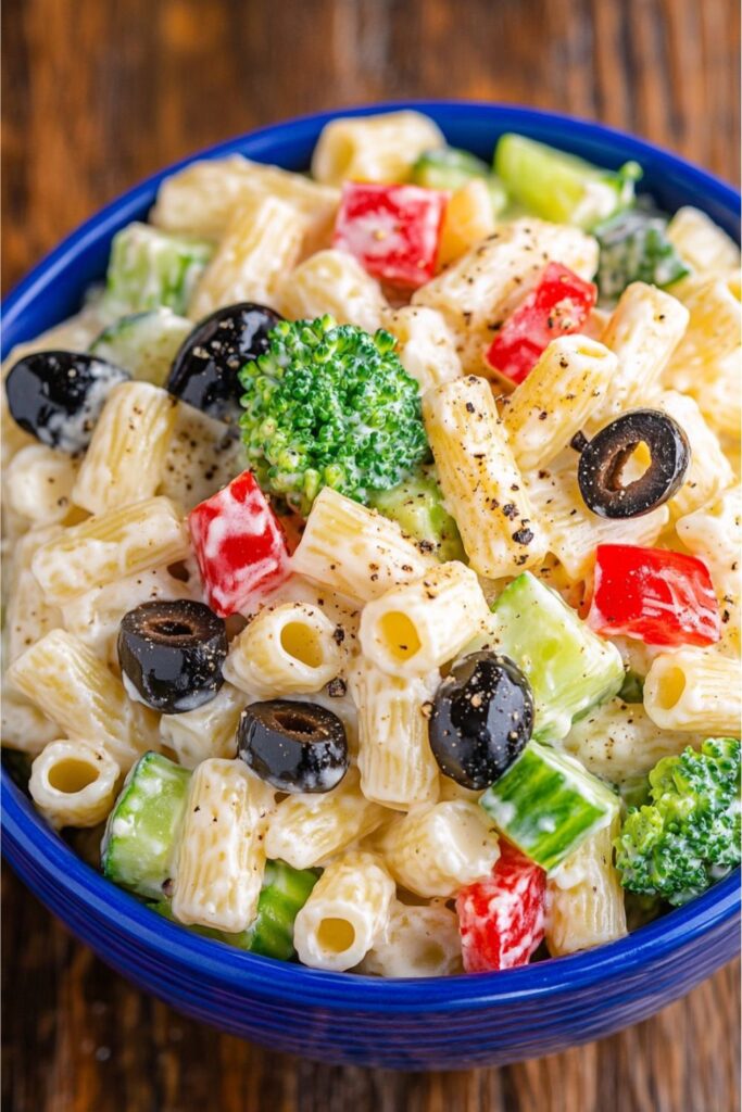 A colorful bowl of creamy macaroni salad with broccoli and olives for party side dishes.