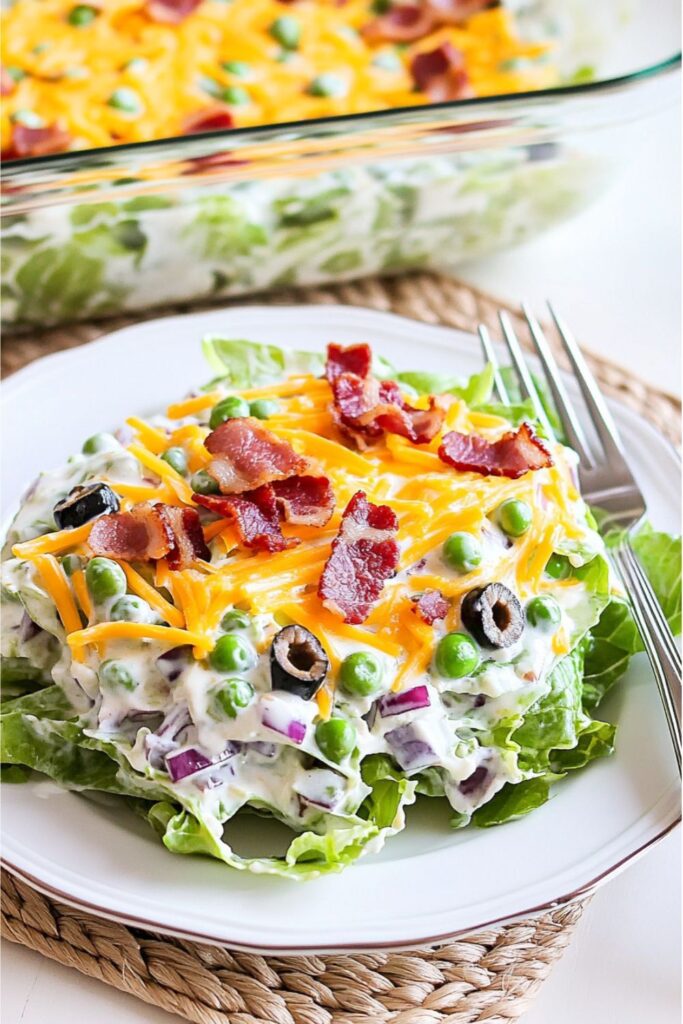 A layered green salad topped with bacon and cheese, served as classic cookout sides.