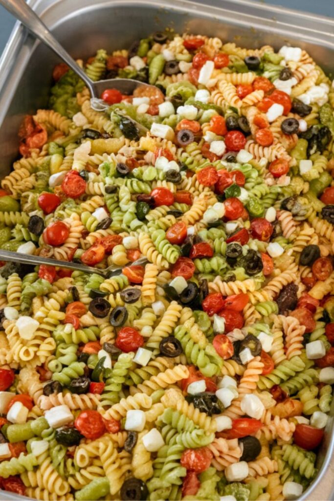 Large tray of multi-colored rotini pasta with olives and tomatoes for cookout sides.