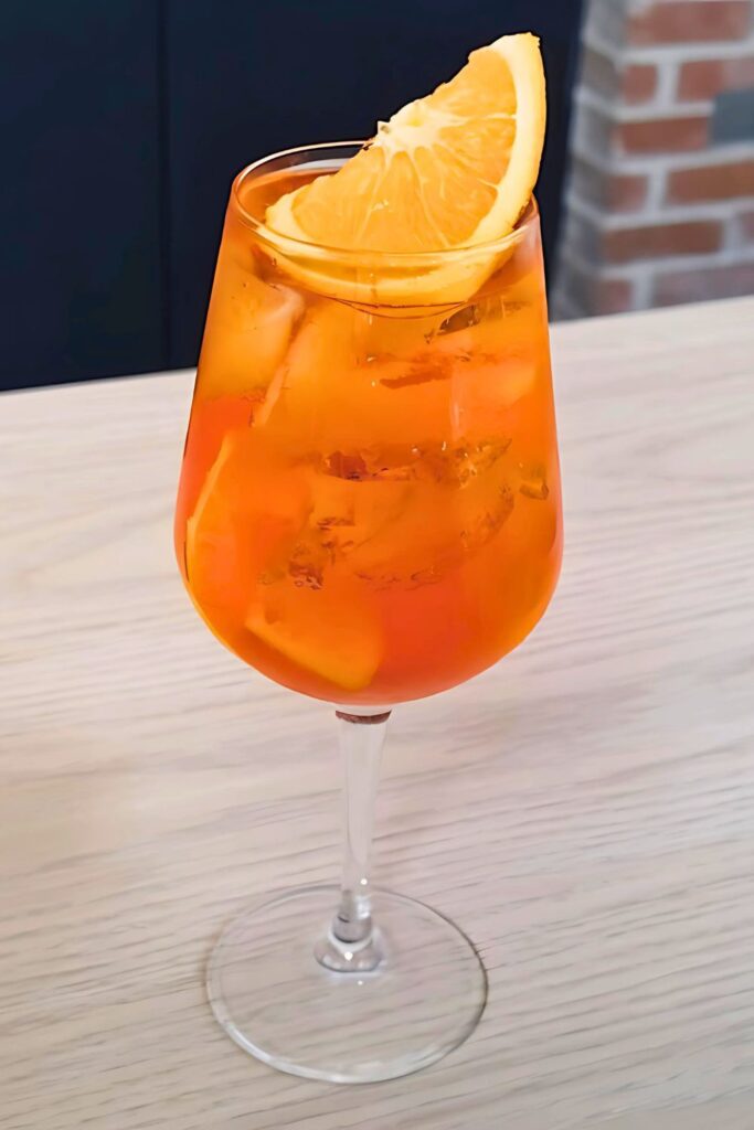 Bright orange Aperol spritz cocktail in a glass with ice and orange slice.