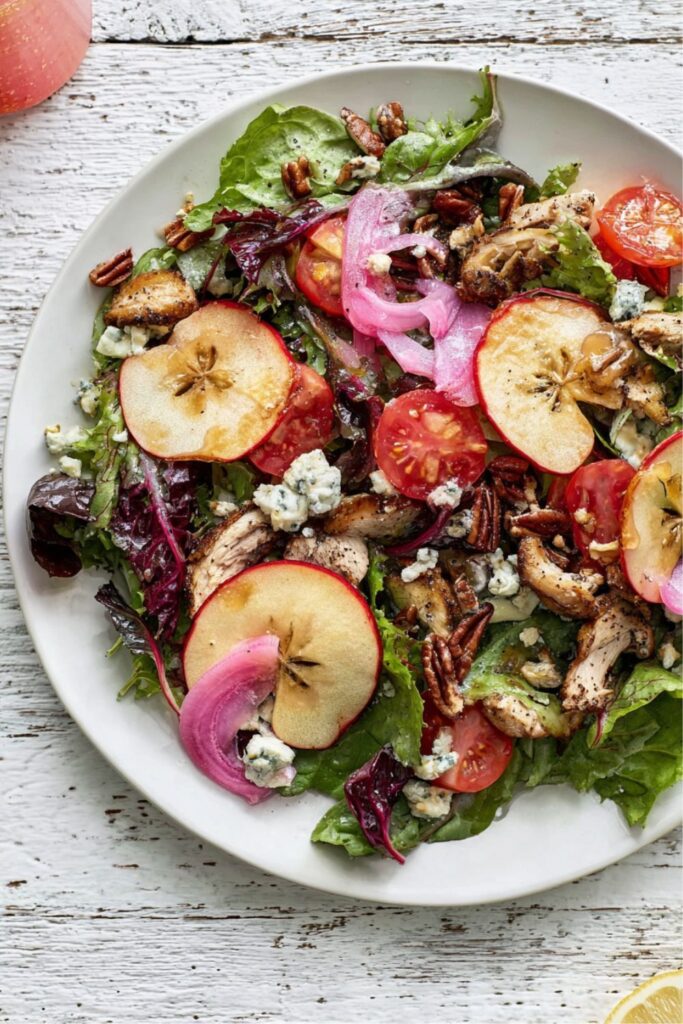 Colorful salad with apple slices, pickled onions, pecans, and greens on plate.