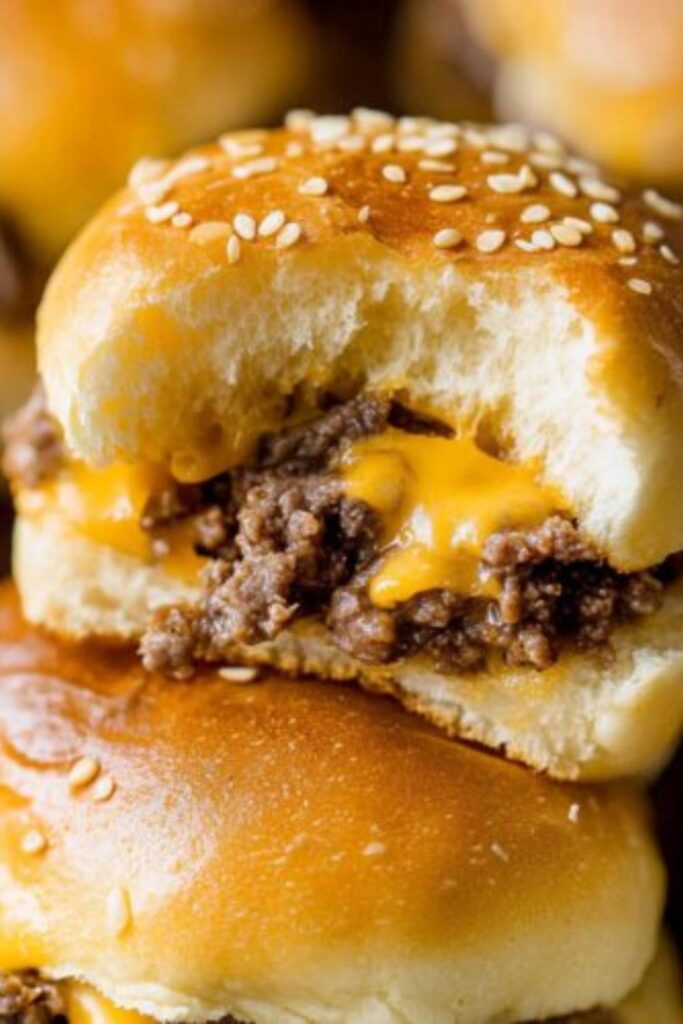 A hand holds a golden-brown cheesy beef slider from a sheet pan.