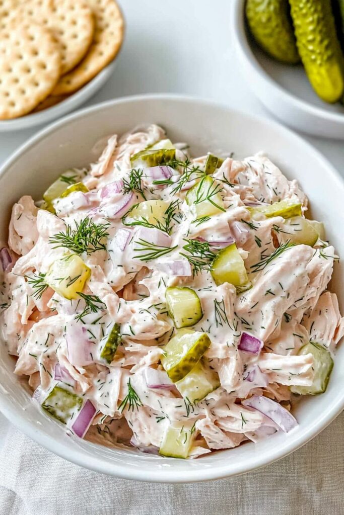 Creamy chicken salad with chopped dill pickles and red onion in a bowl.