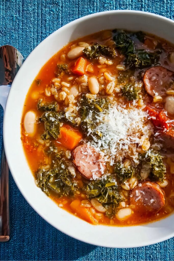 Hearty bowl of Giada De Laurentiis’ house soup with farro, kale, beans, carrots, kielbasa, and grated Parmesan on top.