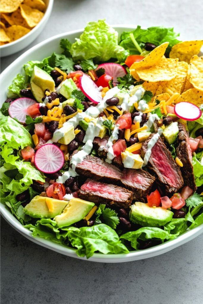 Vibrant taco salad with sliced medium-rare steak, avocado, black beans, and crunchy tortilla chips.