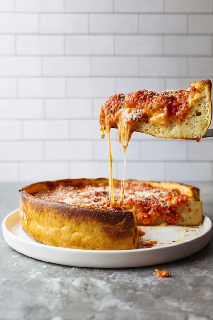 Slice of deep-dish pizza being lifted from the whole pie, showing melted cheese, thick crust, and marinara sauce.