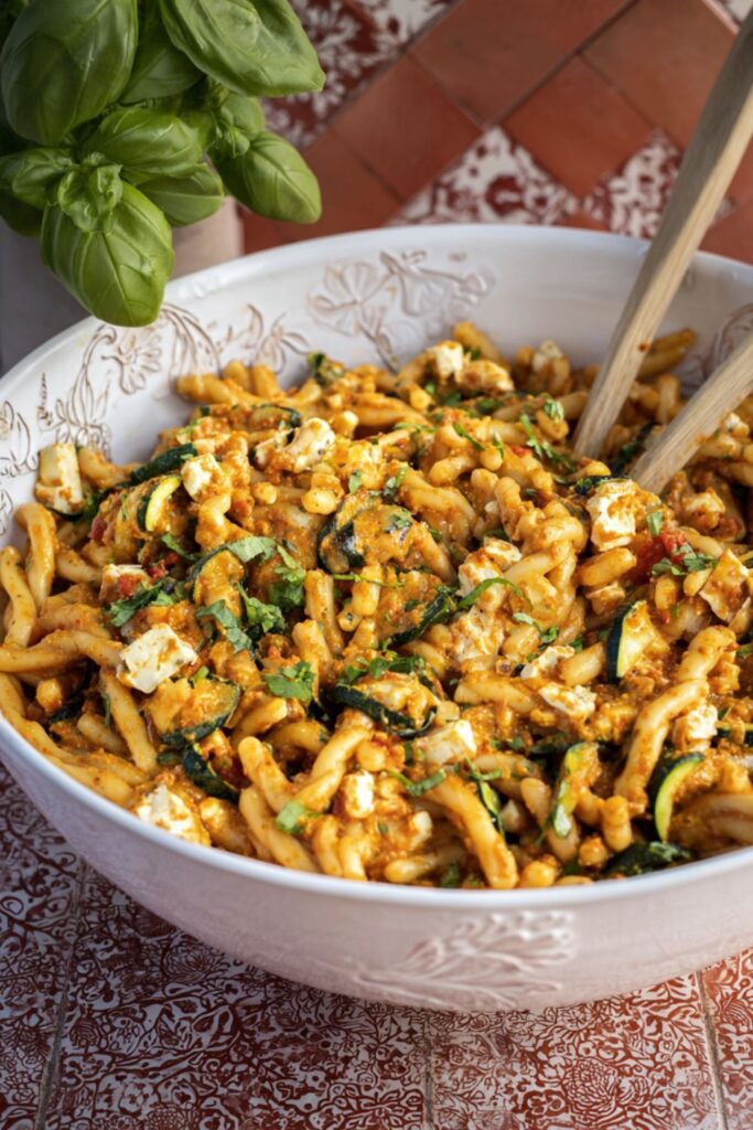Sicilian pesto pasta salad in a large white bowl with roasted vegetables, crumbled feta, and fresh herbs.