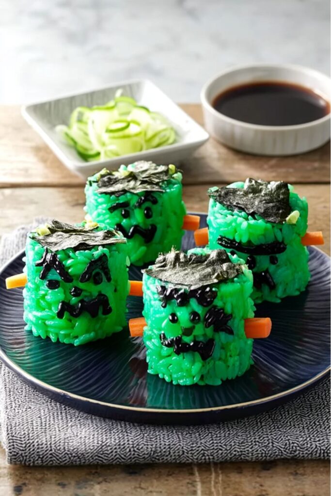 Green-tinted sushi rolls decorated with nori hair, carrot bolts, and wasabi faces to resemble Frankenstein, making them a spooky yet fun option for salty halloween snacks and other halloween food and snacks.