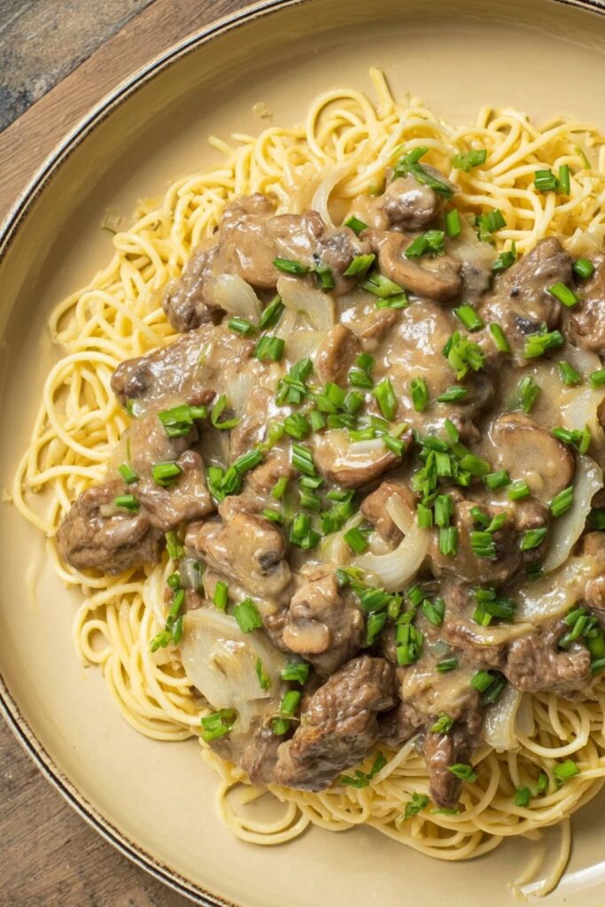 A creamy beef stroganoff with strips of ribeye, sautéed onions, mushrooms, and egg noodles, finished with sour cream sauce and chives, inspired by the best Ina Garten recipes.