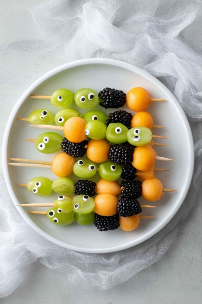 Halloween skewers made with cantaloupe, blackberries, and green grapes decorated with candy eyeballs, arranged as spooky fruit kabobs for a festive Halloween food platter.