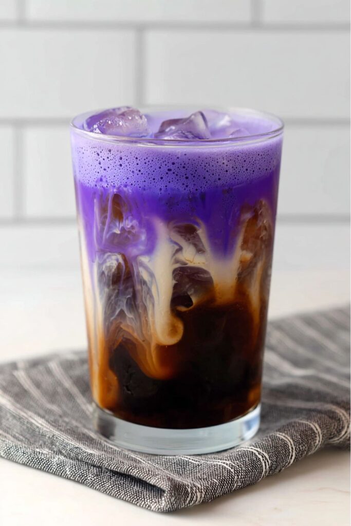 A tall glass of cold brew coffee swirled with purple frothed milk and ice, creating a vibrant and festive drink perfect for Halloween coffee drinks.