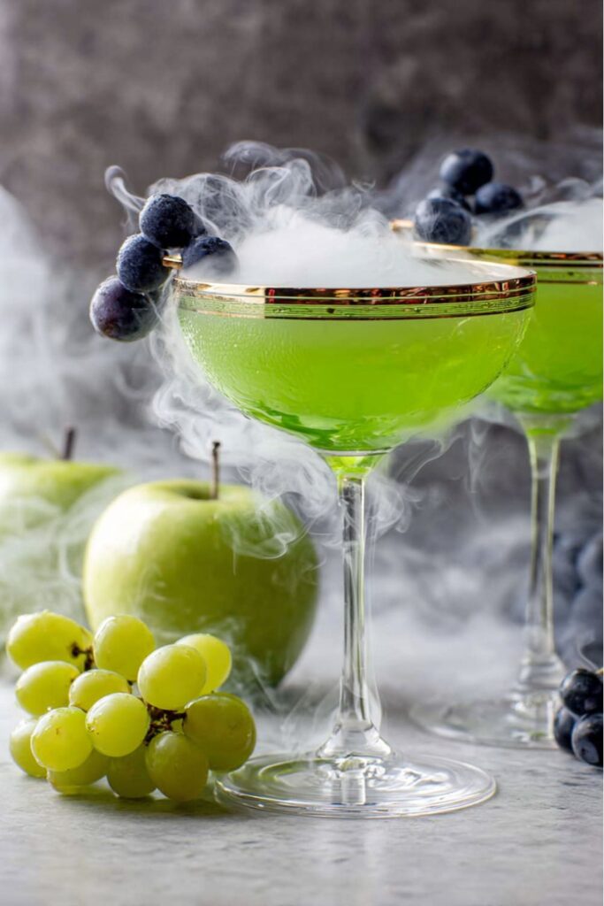 A bright green sour apple martini in a chilled glass, served over ice, making it a bold and spooky choice for Halloween themed drinks.