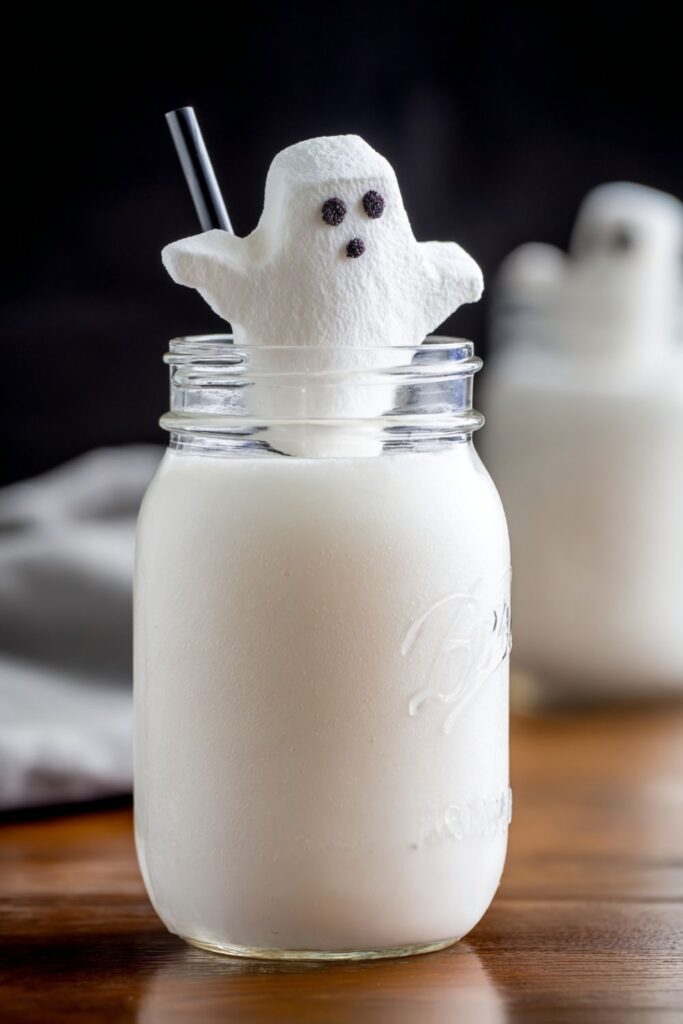 A creamy white Halloween cocktail in a glass topped with lemon-lime soda, garnished with a marshmallow Ghost Peep, perfect for spooky Halloween themed drinks.
