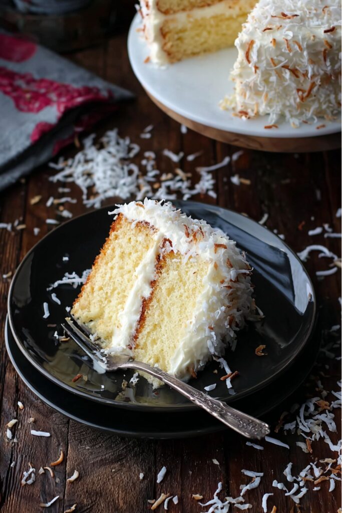A fluffy white coconut cake from Ina Garten recipes, layered with cream cheese frosting and topped with shredded coconut.