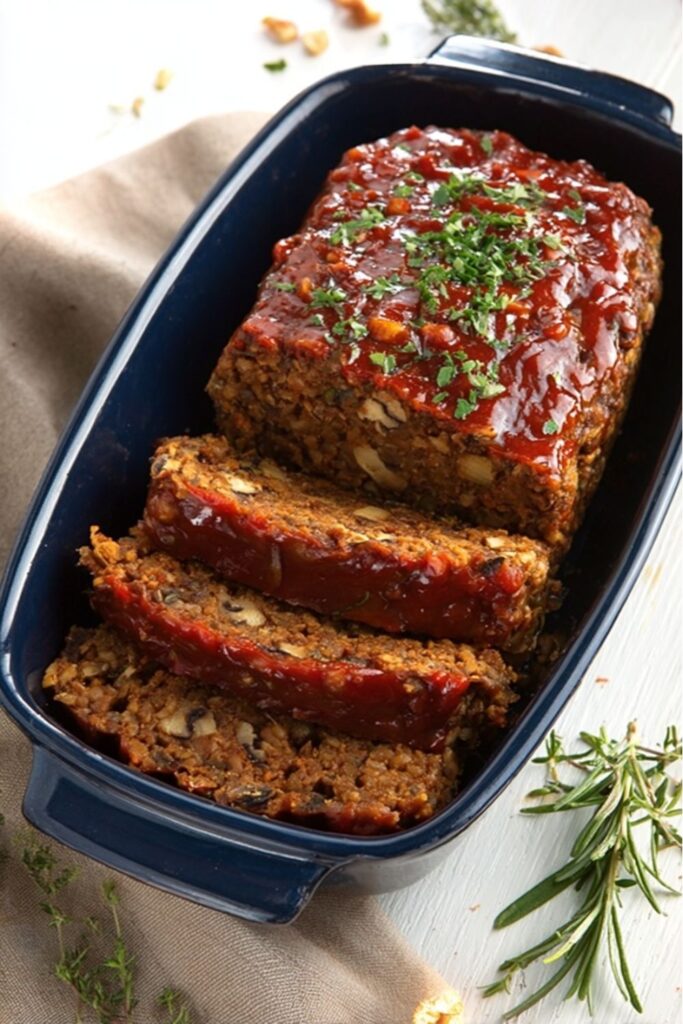 A golden-brown vegan lentil meatloaf glazed with ketchup topping, sliced on a white serving platter and garnished with fresh parsley, perfect for a vegan Thanksgiving dinner spread.