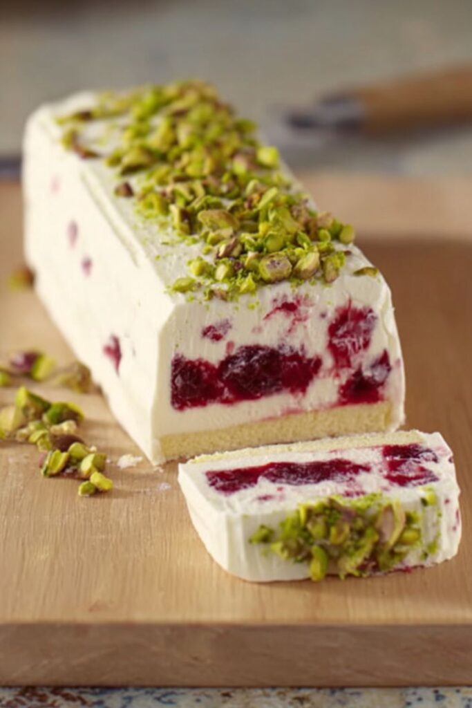 Layered cranberry and limoncello semifreddo in a loaf shape, with Madeira cake at the bottom, garnished with chopped pistachios, a creamy and festive choice for elegant holiday desserts.