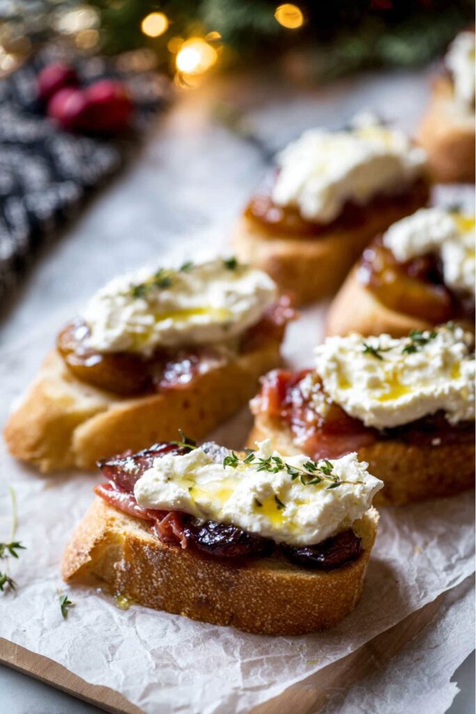 A platter of toasted baguette slices topped with caramelized plums, burrata cheese, prosciutto, and thyme—an elegant appetizer perfect for Italian Christmas dinner ideas.