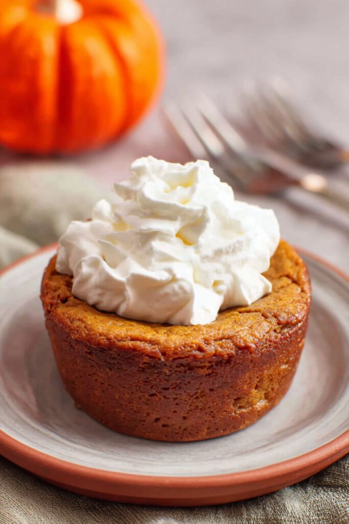 A small pumpkin pie baked in a ramekin with a graham cracker crust, topped with a swirl of whipped cream, perfect for a Thanksgiving for one celebration.