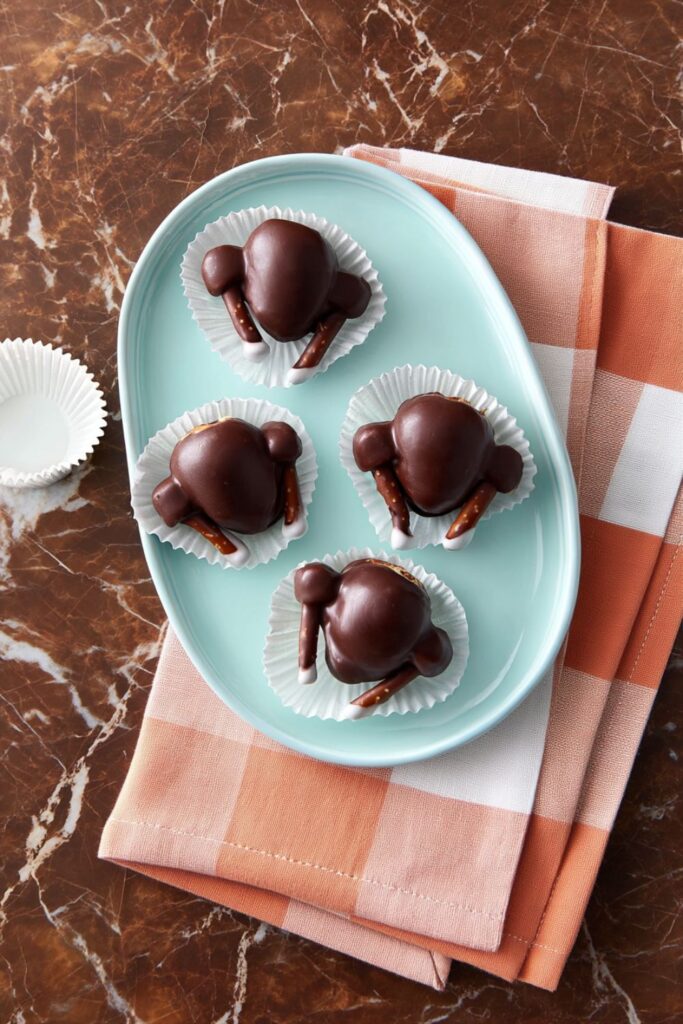 Chocolate-dipped strawberries decorated with pretzel and marshmallow legs, arranged as playful spider-shaped Thanksgiving school treats for kids.
