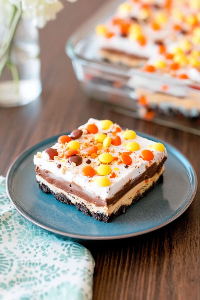Layered peanut butter chocolate dessert topped with whipped cream and crushed Reese’s Pieces, served as festive Thanksgiving school treats for kids.