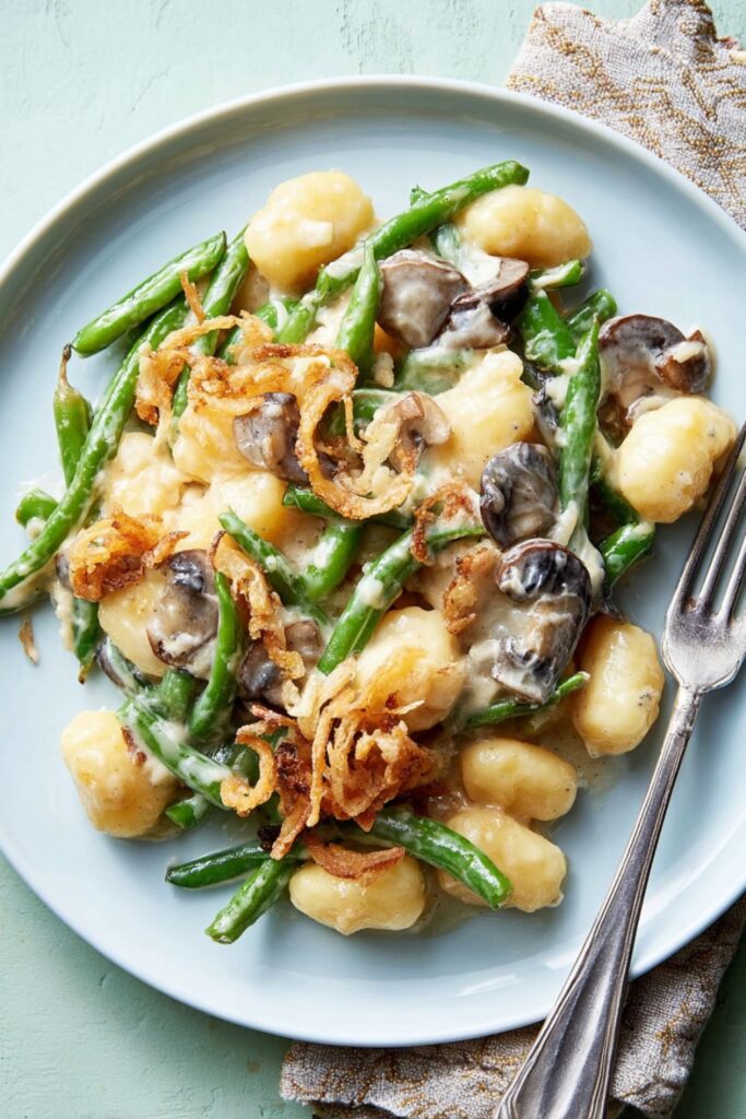 A creamy green bean and mushroom gnocchi casserole baked in a large dish and topped with crispy fried onions, perfect for Thanksgiving side dishes for a crowd.