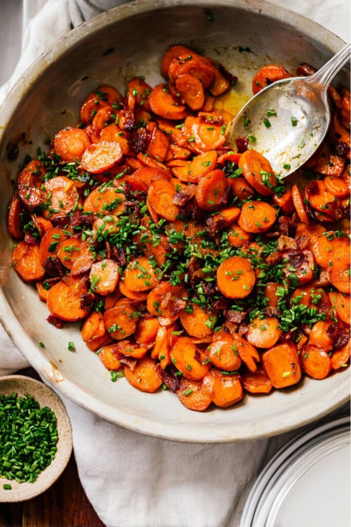 Glazed honey Dijon carrots topped with crispy bacon and fresh chives, served in a skillet as one of the easy Thanksgiving side dishes for a crowd.