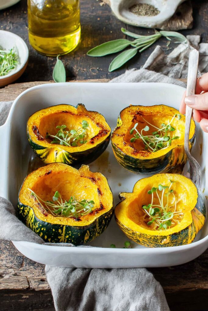 Roasted acorn squash halves drizzled with maple syrup and olive oil, topped with fresh sage and rosemary, served as one of the seasonal vegetable dishes for Thanksgiving.