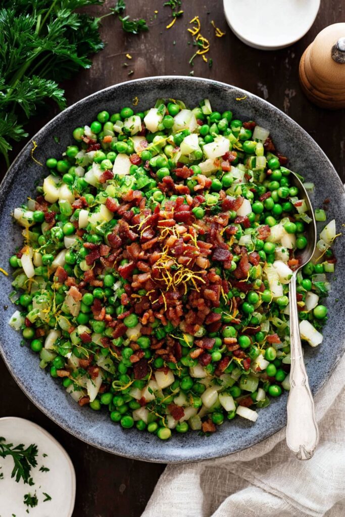 Vibrant green peas sautéed with crispy pancetta, diced pear, and shallots, garnished with lemon zest and parsley, served as one of the unique Thanksgiving side dishes for a crowd.