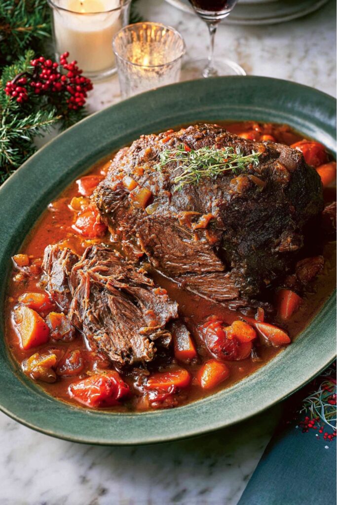 Tender slices of Ina Garten’s company pot roast from Barefoot Contessa Christmas recipes, served with a thick red wine sauce and roasted vegetables on a marble countertop.