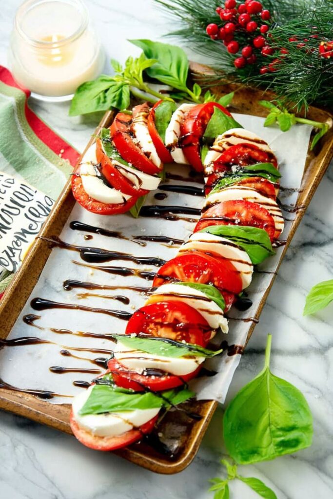​A visually striking Caprese salad arranged as Christmas themed snacks on a gold serving tray lined with parchment paper. Slices of fresh tomato, mozzarella, and basil leaves are layered and arranged in the shape of a large candy cane, drizzled with a balsamic glaze. This makes for an Impressive Christmas Dessert (or appetizer) idea.