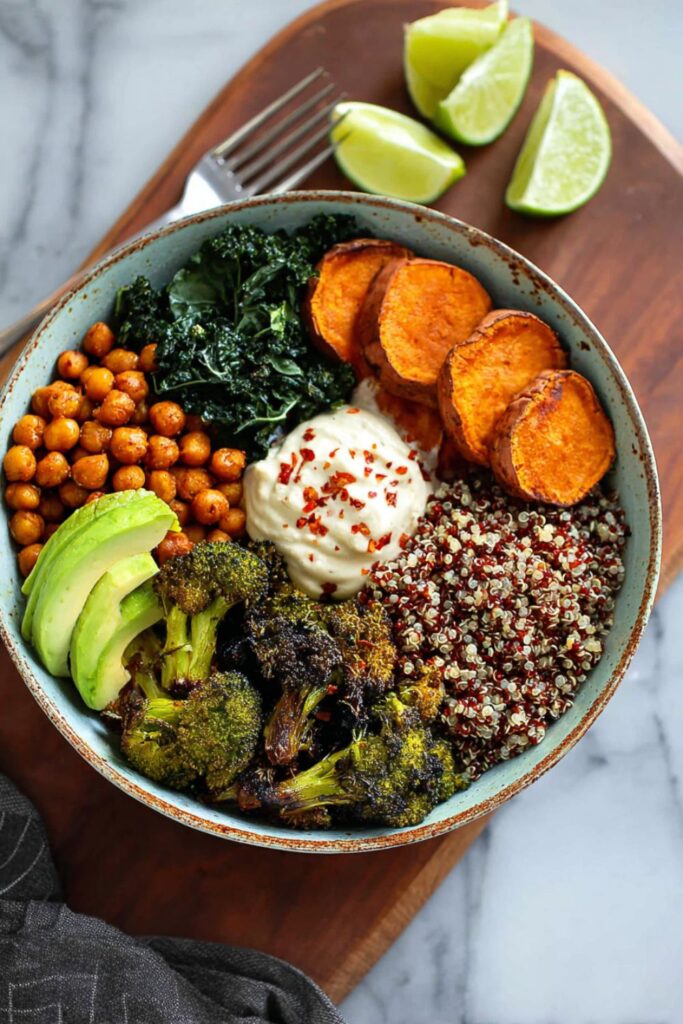 High Protein Veganuary Recipes: A colorful quinoa bowl with roasted sweet potato slices, chickpeas, charred broccoli, steamed kale, sliced avocado, and a dollop of white sauce.