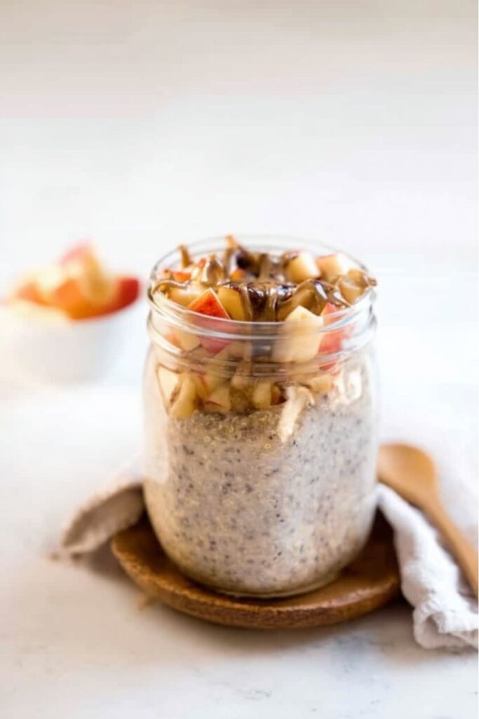 Overnight Quinoa Breakfast jar with a creamy quinoa and chia seed mixture, topped with diced apples and a drizzle of caramel or nut butter, sitting on a wooden coaster.
