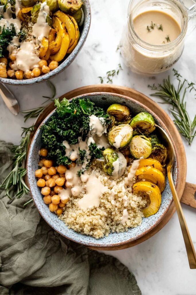Quinoa Recipes for Veganuary: A cozy vegan bowl featuring quinoa, roasted delicata squash, Brussels sprouts, chickpeas, kale, and a creamy tan dressing, with a jar of dressing nearby.