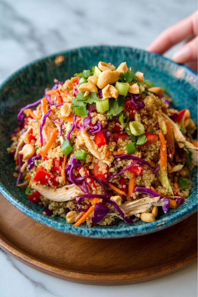 A close-up, high-angle view of a teal bowl filled with a colorful and crunchy Quinoa Salad Meal Prep mix of quinoa, shredded chicken, purple cabbage, carrots, red peppers, and green onions, topped with chopped peanuts.