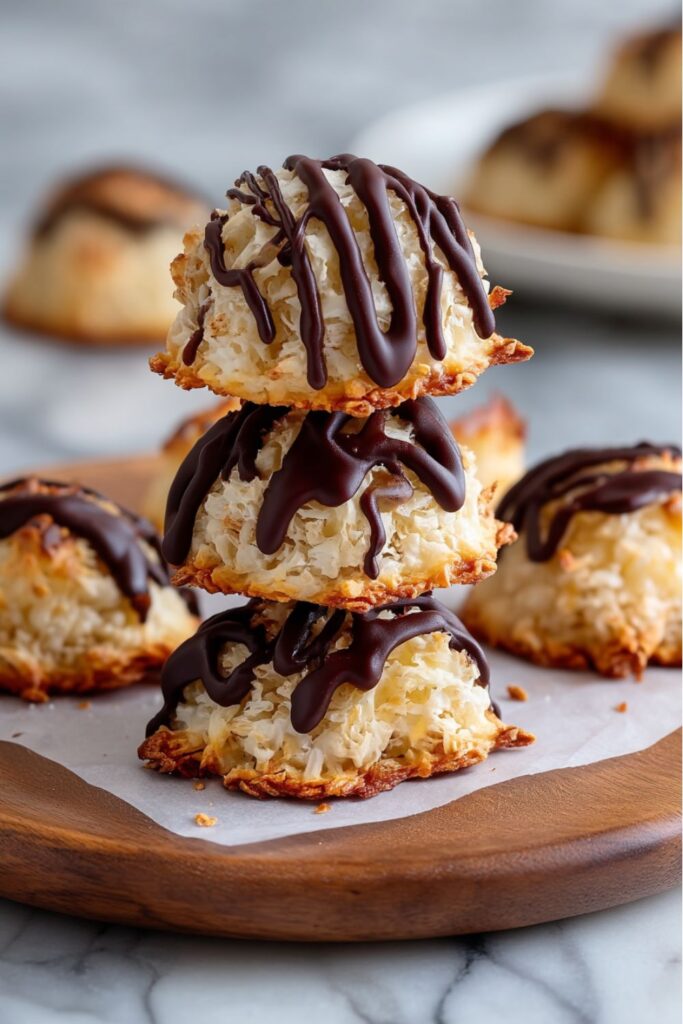 A stack of three golden-brown coconut macaroons, each one generously drizzled with dark melted chocolate, sitting on a small wooden serving plate, representing a festive and naturally gluten free dessert.