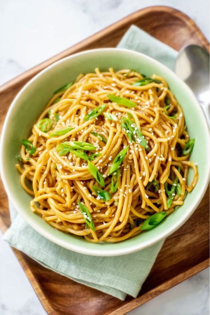 A bowl of glossy, dark brown sesame spaghetti noodles tossed with sliced green scallions and white sesame seeds, showcasing a fast option for Vegan Dinners.