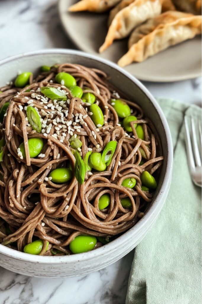A bowl of dark soba noodles tossed with bright green edamame and topped with sliced green onions and sesame seeds, representing fast Veganuary Recipes perfect for a quick dinner.