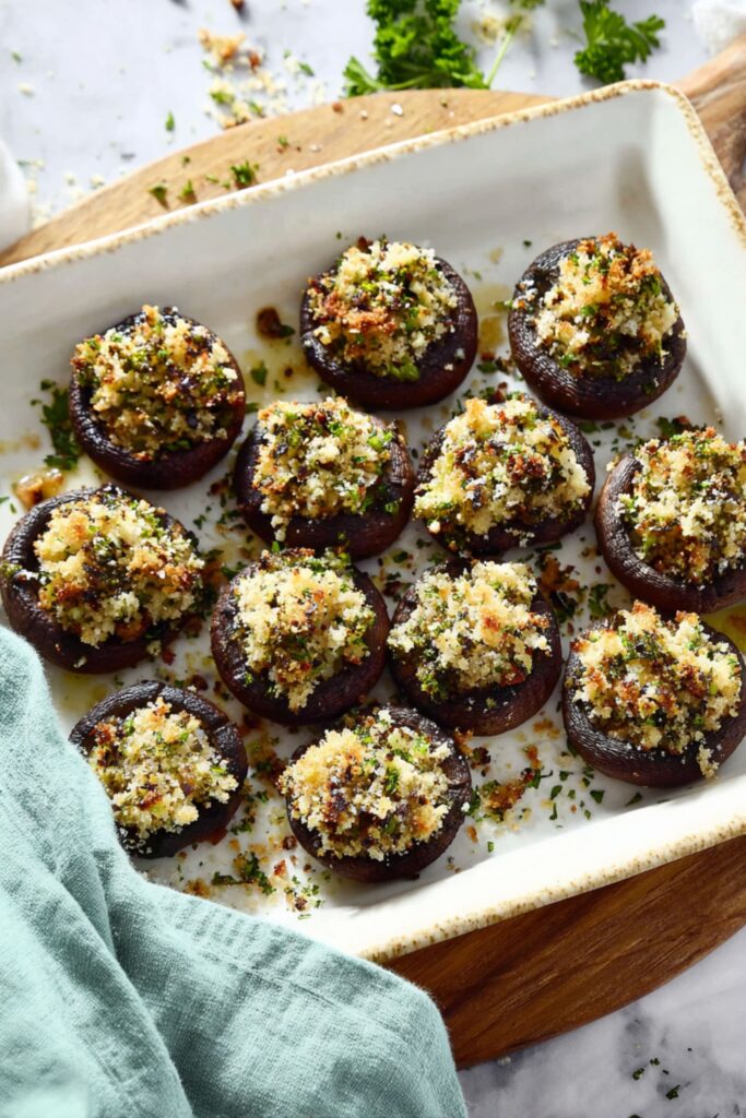 Twelve small portobello mushroom caps stuffed with a golden-brown breadcrumb and parmesan mixture, garnished with fresh parsley as easy vegetarian appetizers finger foods.