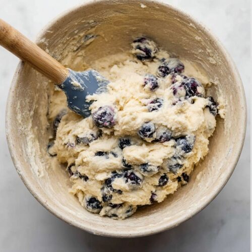 A bowl of chunky scone dough filled with fresh blueberries being mixed with a spatula.