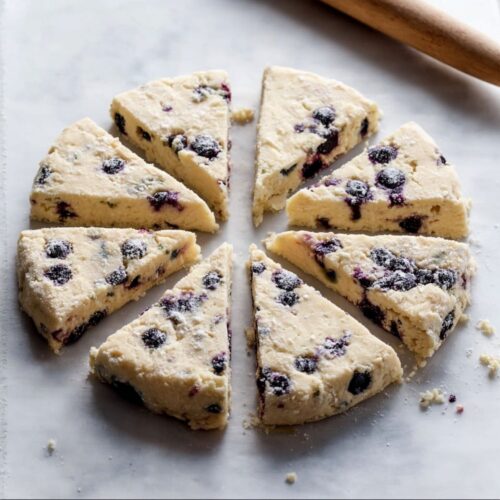 Unbaked blueberry scones cut into eight wedges on a floured surface with a rolling pin.