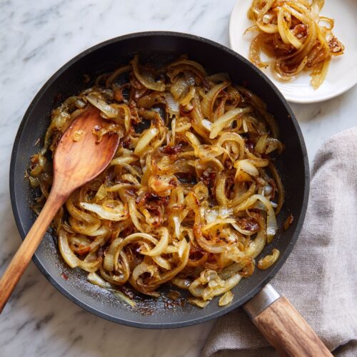 Top-down view of golden caramelized onions in a dark skillet on a marble surface.