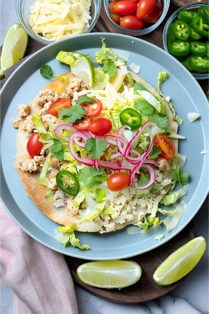 Chicken tostada with lettuce, tomatoes, jalapeños, and lime wedges, lean cinco de mayo dinner ideas.