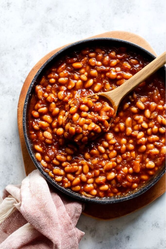 A wooden spoon scooping bubbly baked beans from a skillet, representing Father Day Food Ideas.