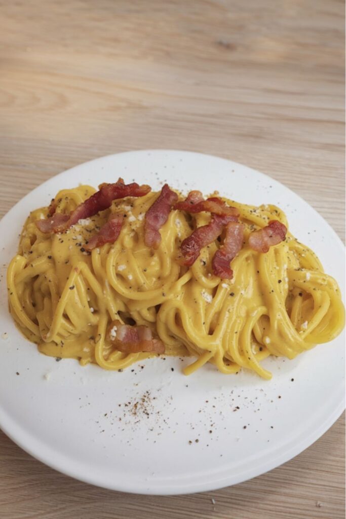 Creamy egg and pecorino romano spaghetti topped with crispy guanciale on a plate.