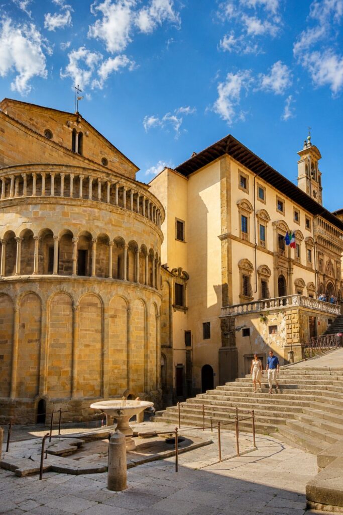 Arezzo’s stone apse, broad steps, palazzo, and clock tower under a bright blue sky