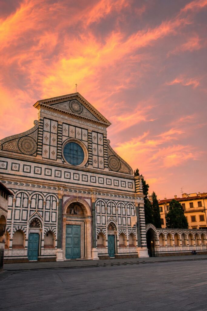 Basilica of Santa Maria Novella façade glowing under orange sunset clouds in Florence