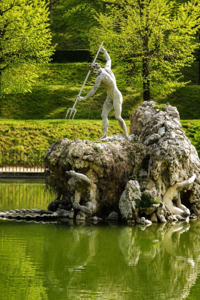 White Neptune statue and rocky island reflected in a green pond at Boboli Gardens