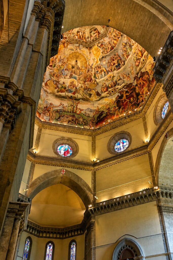 Interior view of Brunelleschi’s Dome with frescoed ceiling, stone arches, and stained glass