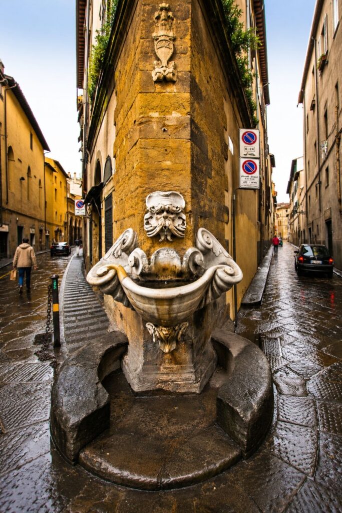 Wet stone street and ornate fountain in Florence’s Oltrarno near historic yellow buildings